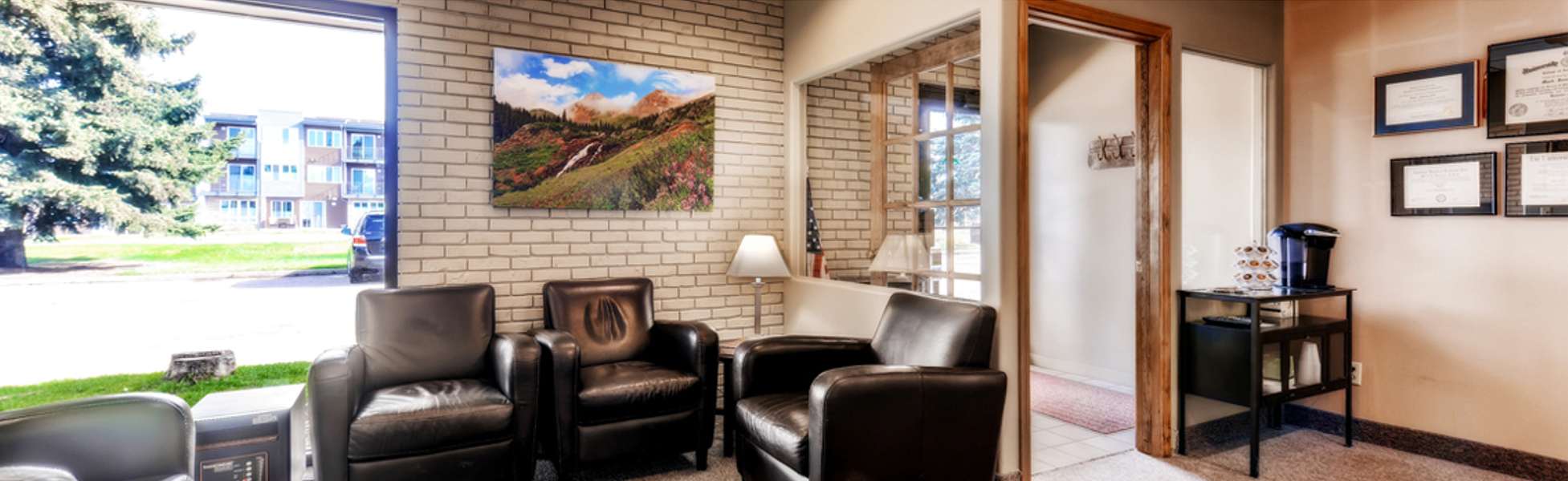 Bright waiting room at Gunbarrel Family Dentistry with leather chairs, brick wall, and mountain artwork
