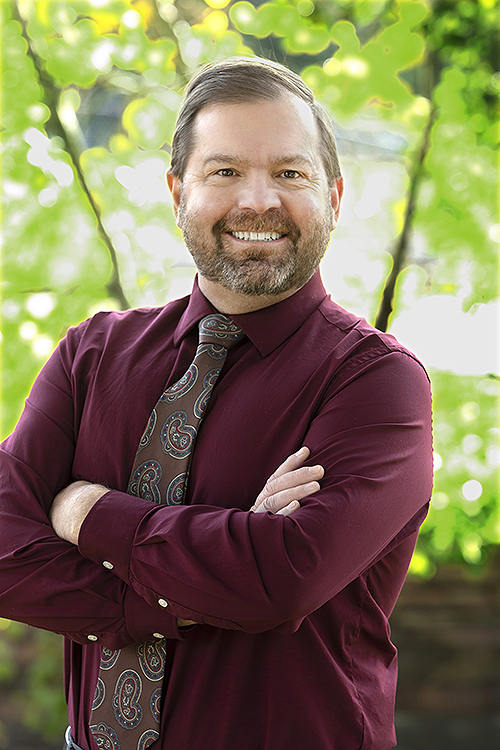 Portrait of Dr. Harald Joesaar smiling outdoors in a maroon shirt and patterned tie